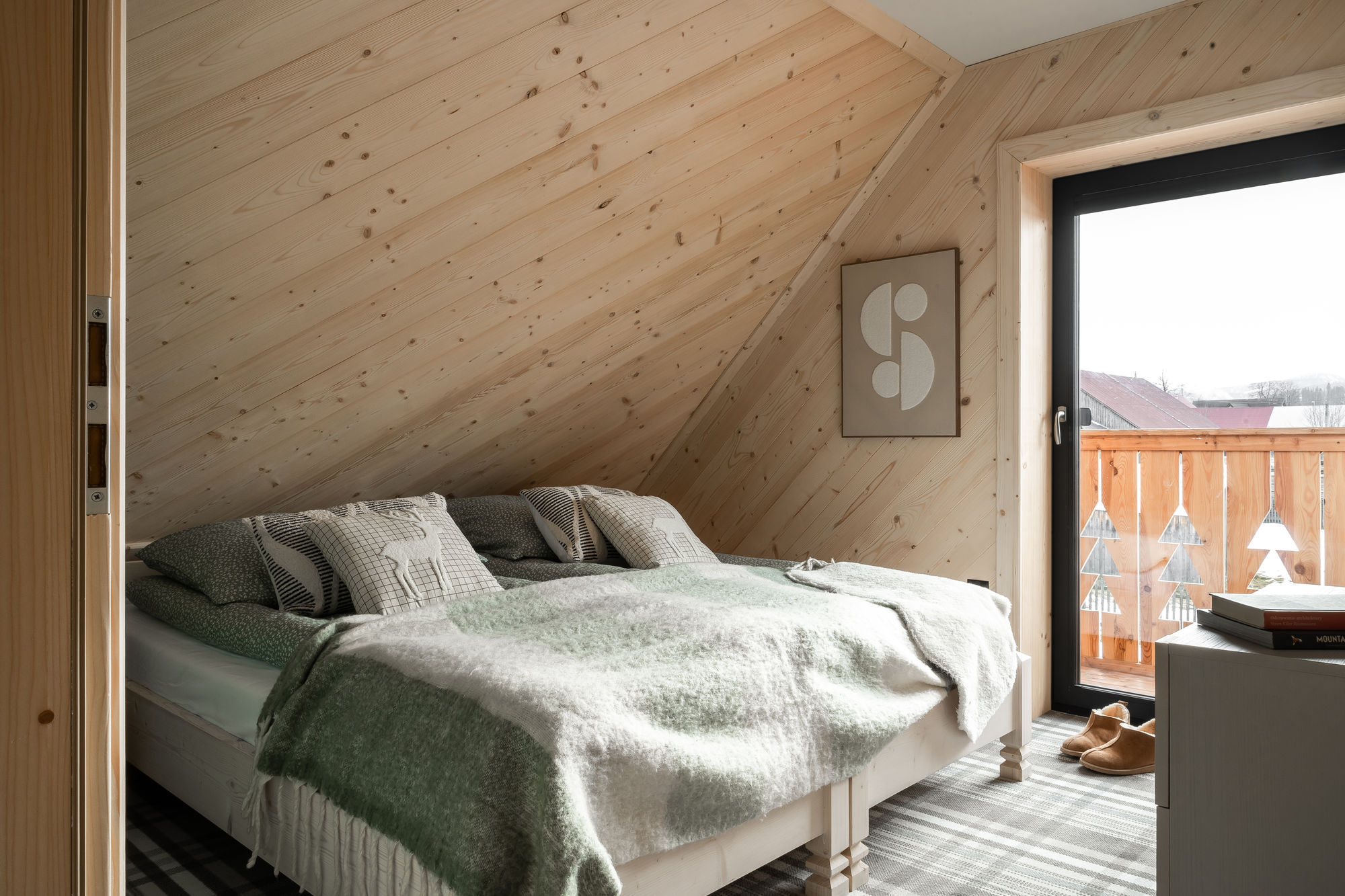 Jasna sypialnia z drewnianą skosową ścianą, łóżkiem i wyjściem na balkon