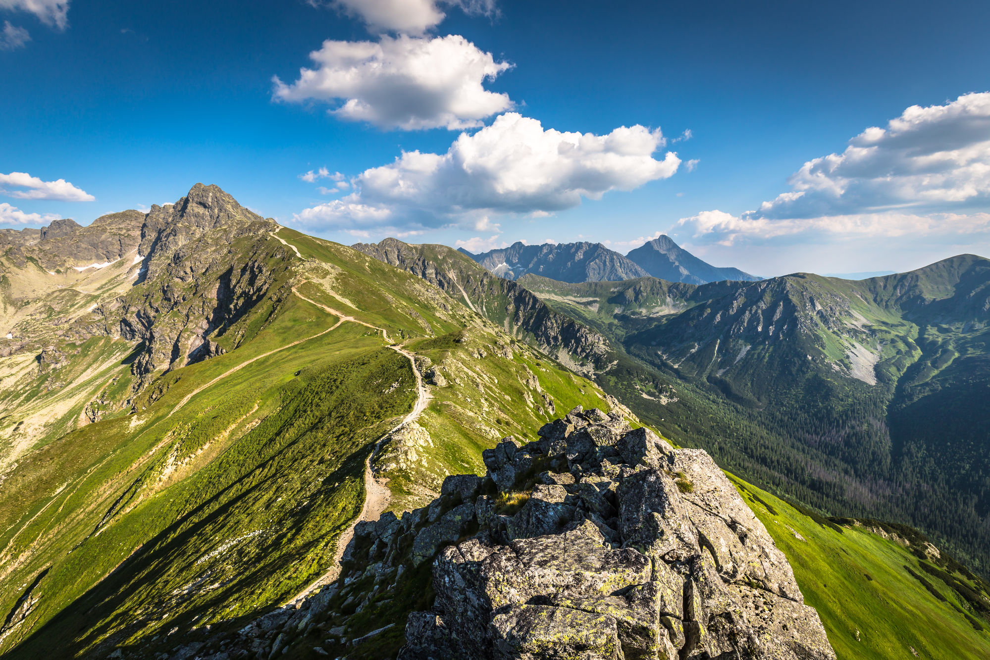 Panorama górskich grani, zielonych dolin i skalistych szczytów pod błękitnym niebem z chmurami