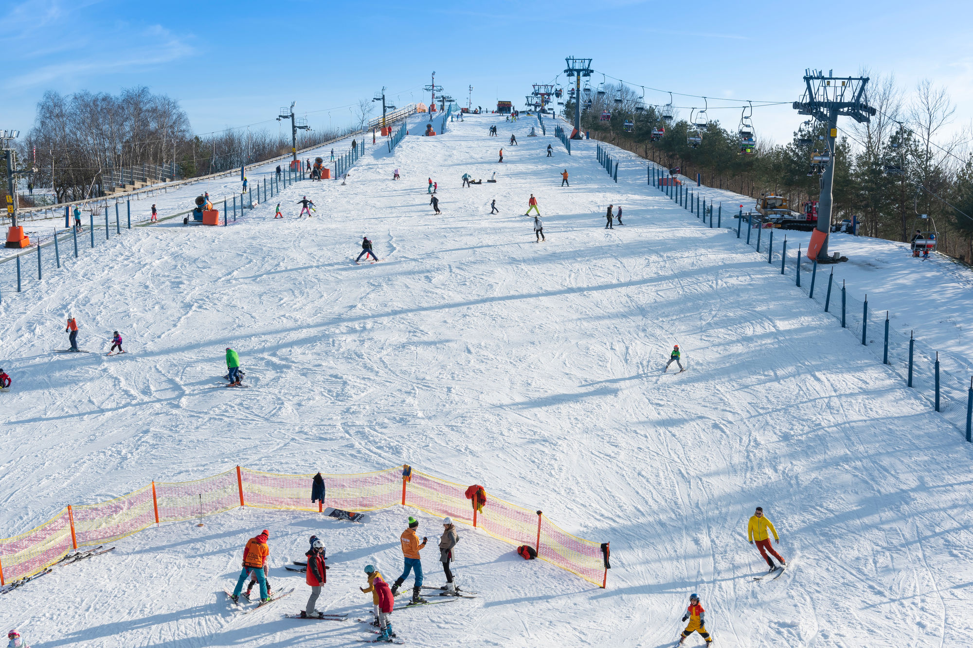 Narciarze i snowboardziści na szerokim, ośnieżonym stoku z wyciągiem krzesełkowym