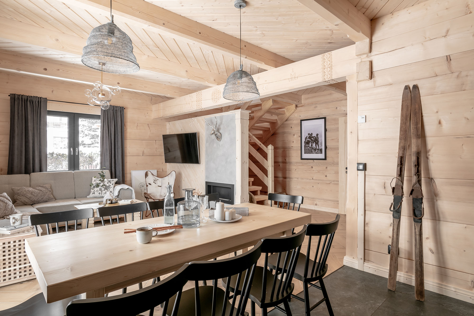 Jasny drewniany salon z jadalnią, kominkiem, schodami i nartami opartymi o ścianę