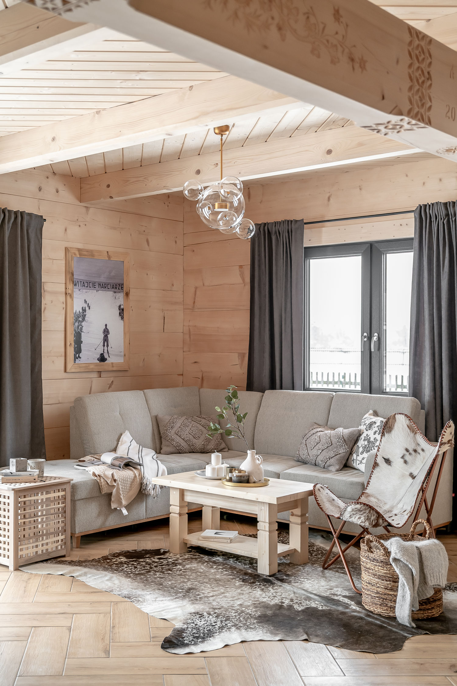 Przytulny salon w drewnianym wnętrzu, z jasną sofą, stolikiem, futrzanym fotelem i dużym oknem